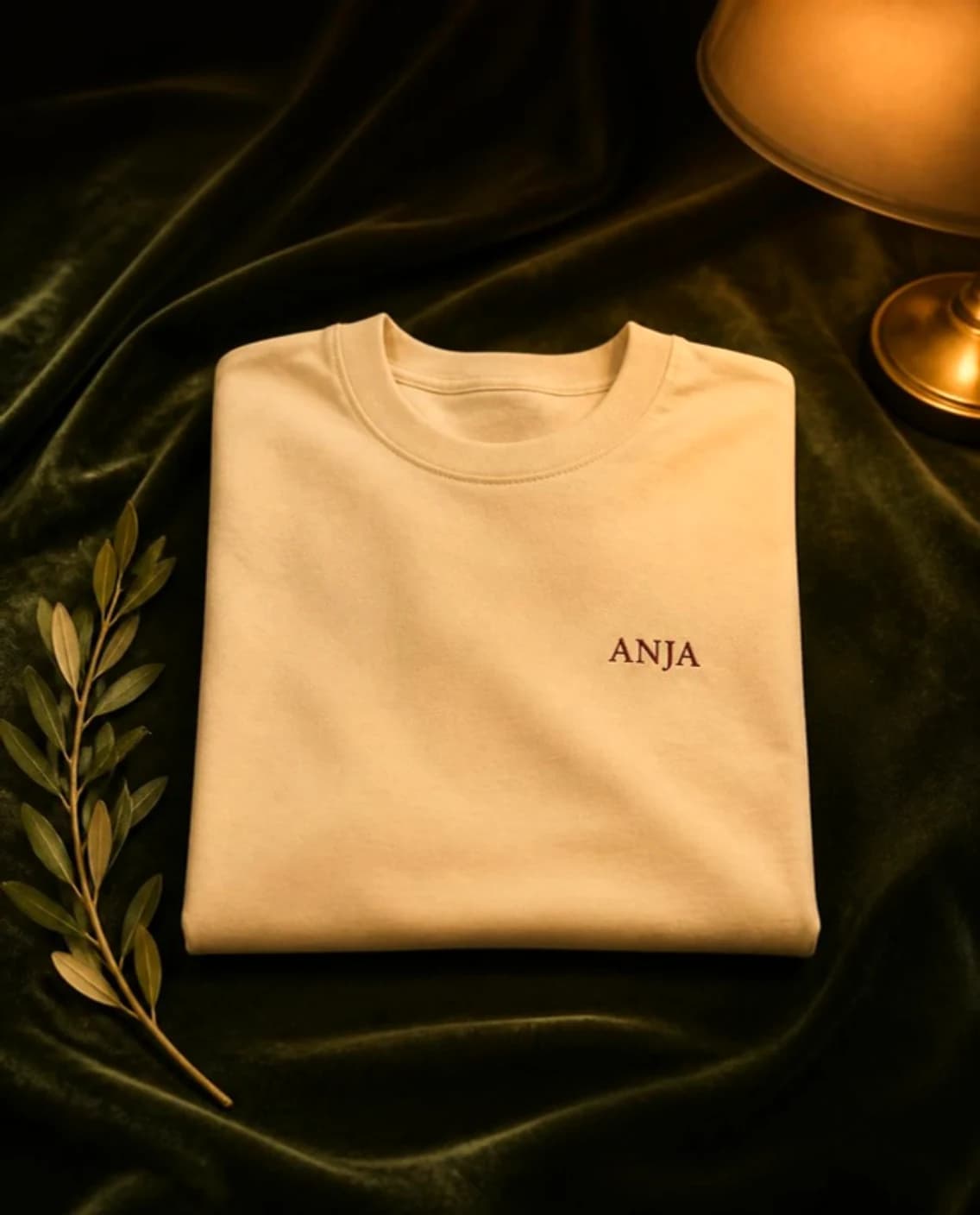 Anja Tee in parchment, folded on green velvet, with ANJA embroidered in oxblood on the chest
