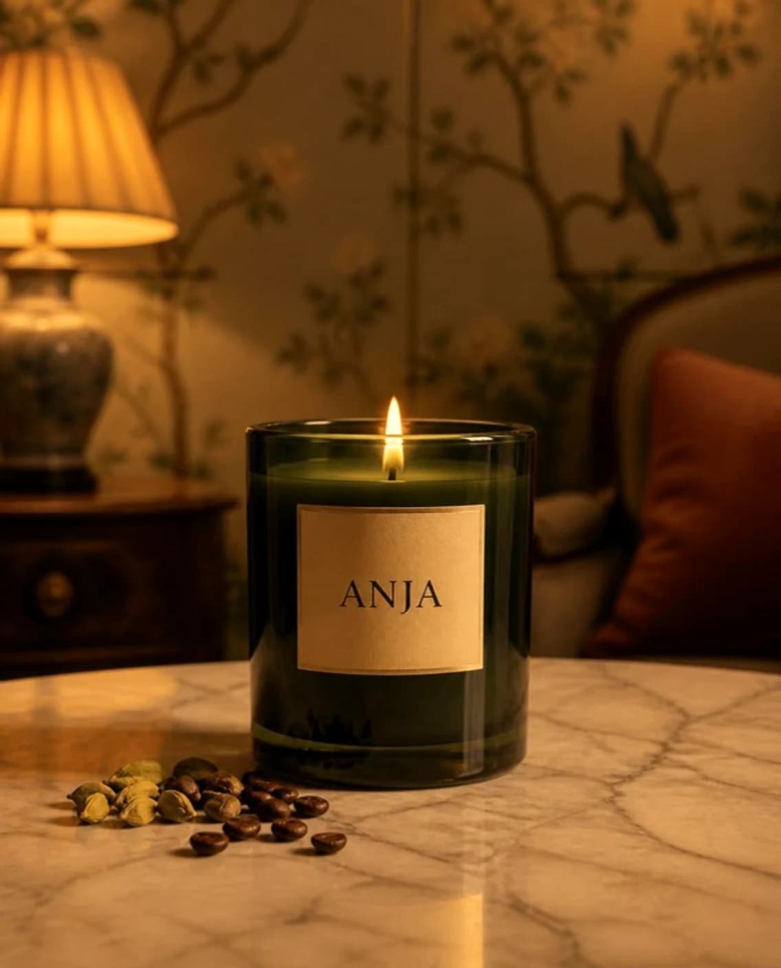 Lit candle in a green glass jar with an ANJA label, with cardamom and coffee beans on marble